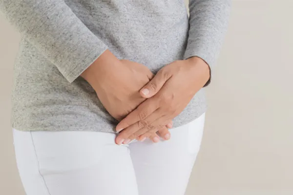 Close up of a woman in a gray shirt and white pants holding her hands below her abdomen in discomfort. Get treatment for fibroids from Deborah Wilson, M.D. & Associates in Scottsdale.
