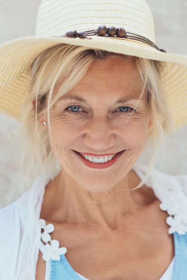 A beautiful, smiling older woman with blonde hair and a sunhat, happy with menopause treatment from Deborah Wilson, M.D. & Associates in Scottsdale.