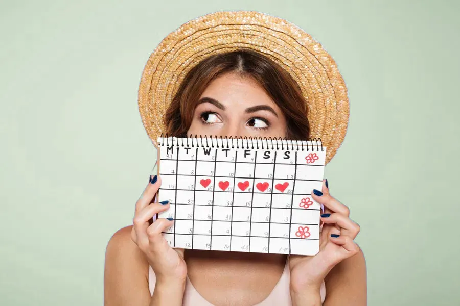 A woman in a straw hat holds a calendar with several days marked off in front of her nose and mouth. Get treatment for menstrual dysfunction from Deborah Wilson, M.D. & Associates in Scottsdale.