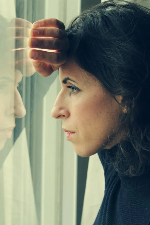 A brunette woman in a thin dark turtleneck looks out the window with a serious expression, suffering from PCOS. Get treatment for Polycistic Ovarian Syndrome/PCOS from Deborah Wilson, M.D. & Associates in Scottsdale.