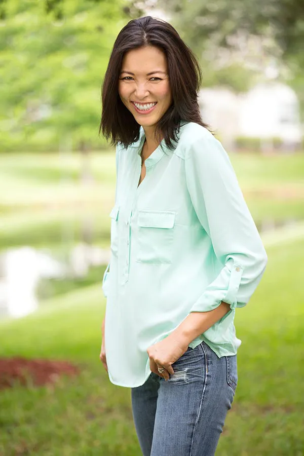 A middle-aged brunette woman in a light green button-up shirt stands outside smiling, happy with her perimenopause treatment from Deborah Wilson, M.D. & Associates in Scottsdale.
